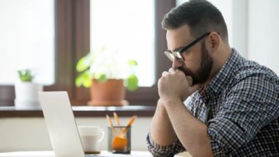 A man looks at his laptop waiting in anticipation.