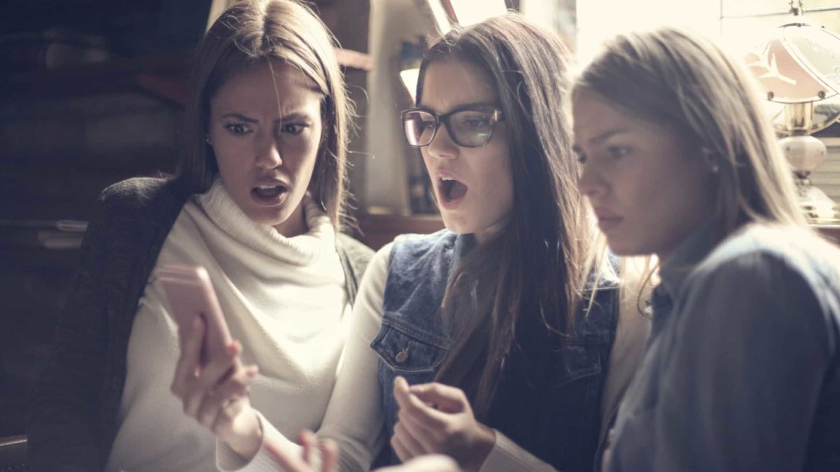 Three woman look shocked around mobile phone.