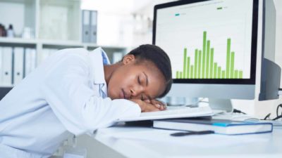 A tired healthcare or lab worker sleeps on her desk