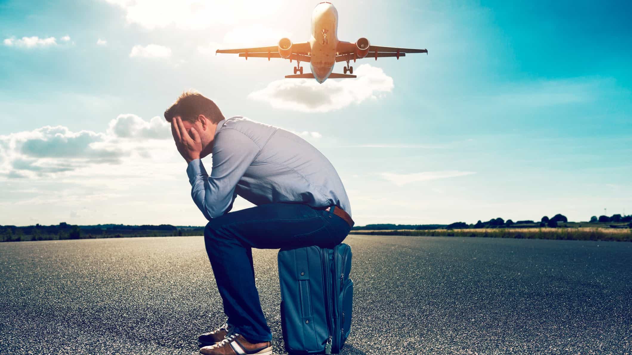 ASX 200 travel shares A man sits on a suitcase with his head in his hands as a plane flies overhead