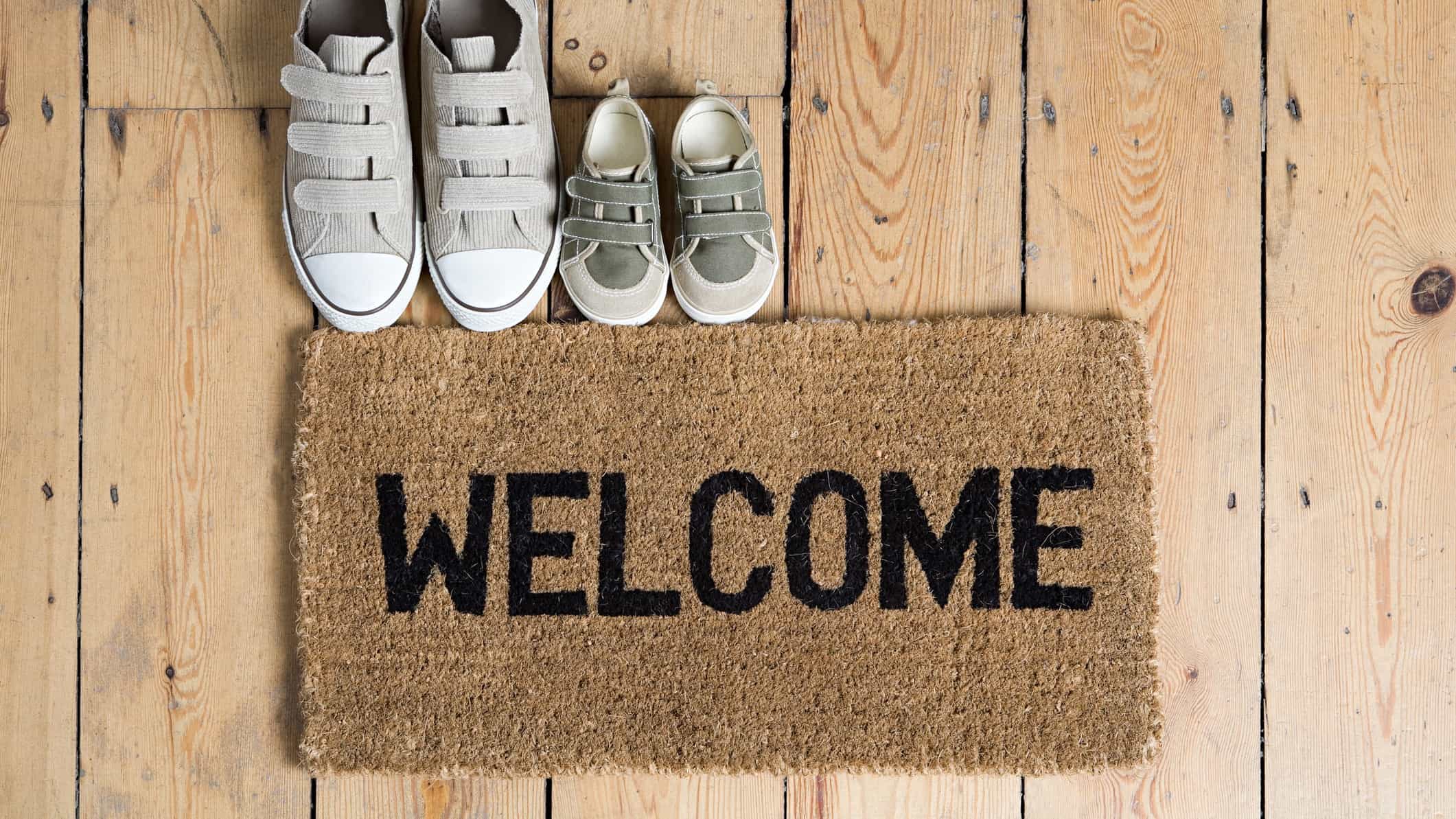 Two pairs of shoes lined up beside a door mat that says the word 'welcome'