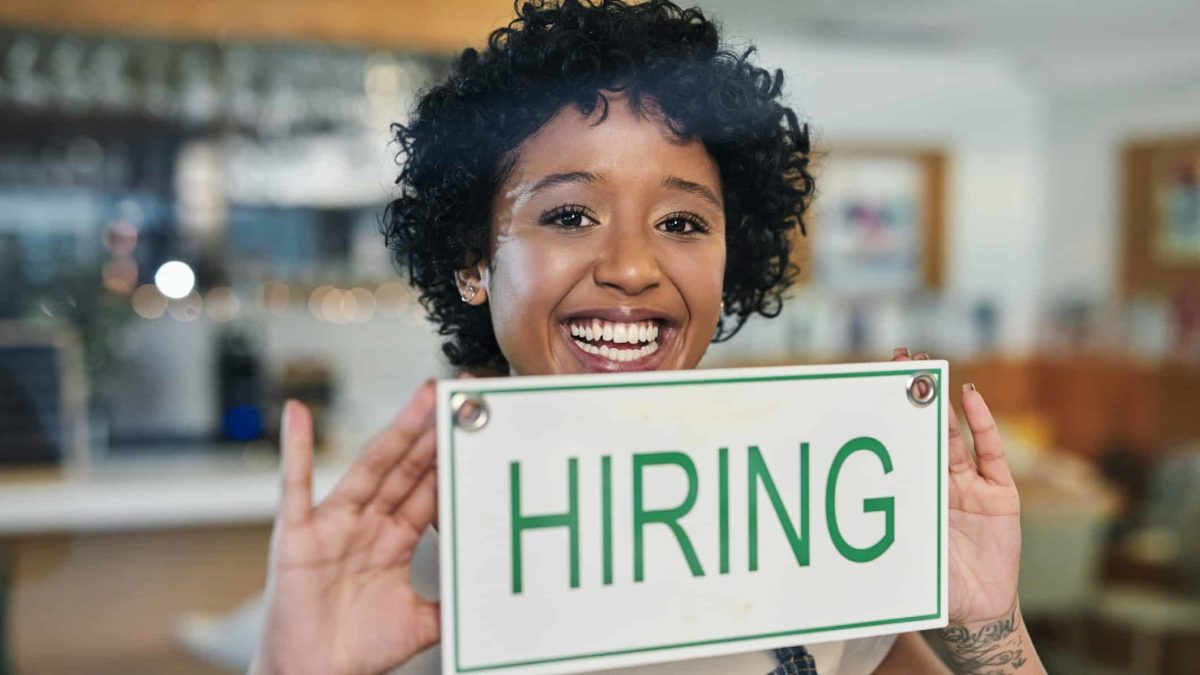 woman holding 'hiring' sign in shop