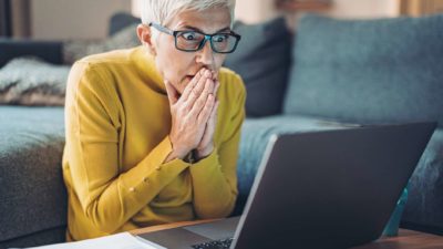 A woman looks in anticipation at her laptop, watching eagerly.