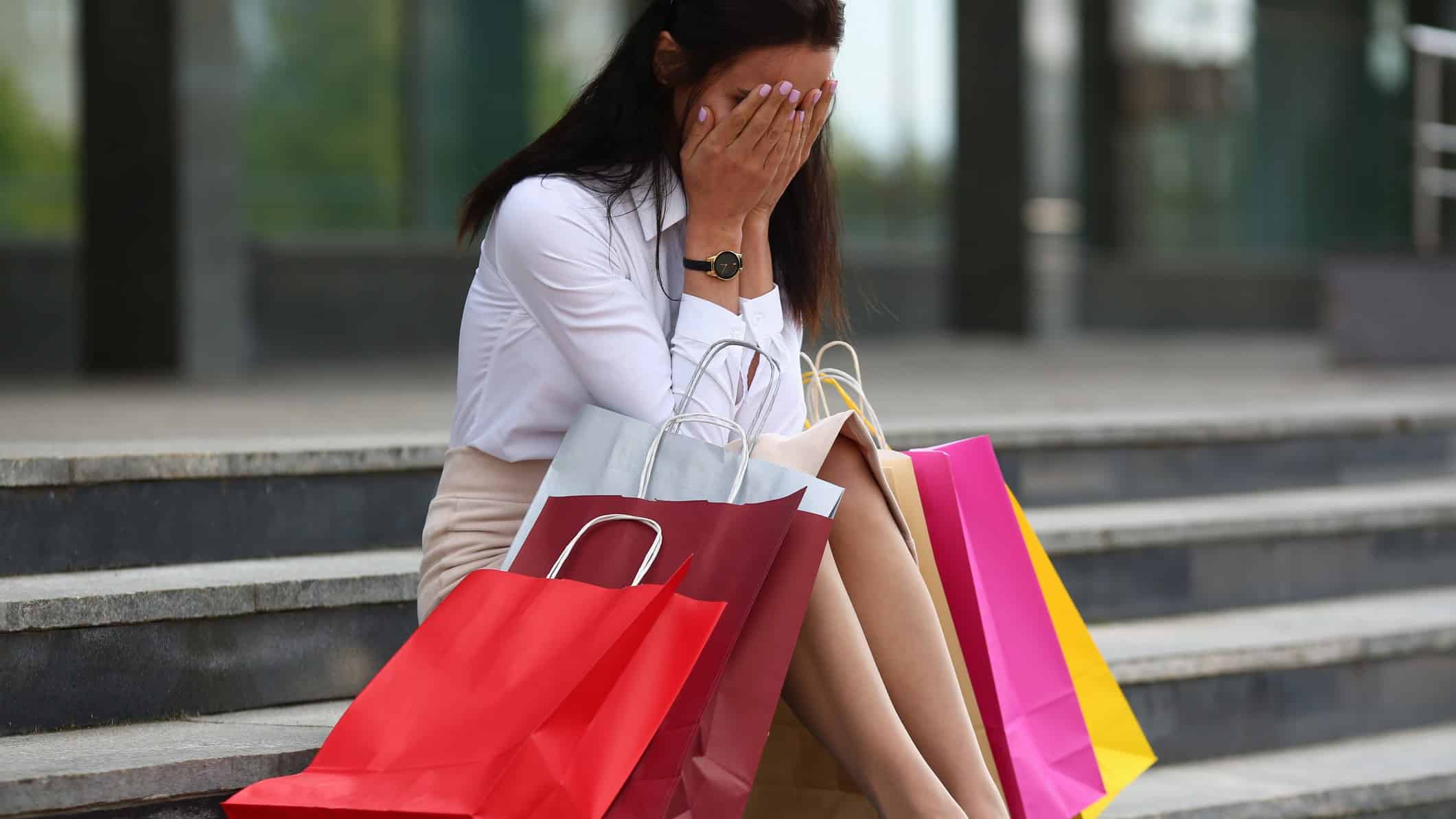 woman with shopping bags sitting on steps with head in hands