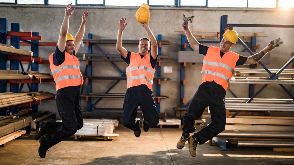 Three workers jump in the air at a steel factory.