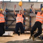 Three workers jump in the air at a steel factory.