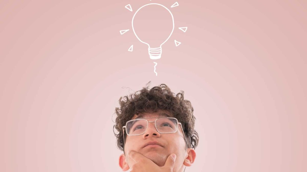 A youthful man looks up thoughtfully at a light bulb above his head.