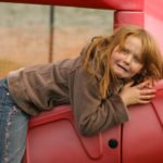 A young girls clings in fright to a big red slide.