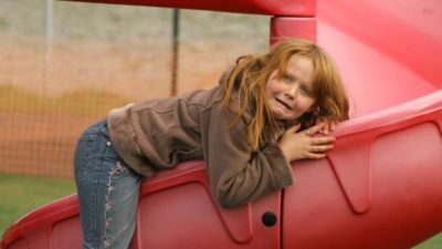 A young girls clings in fright to a big red slide.