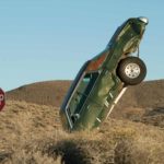 An old rusted car has nose dived from the sky to crash in the barren desert.