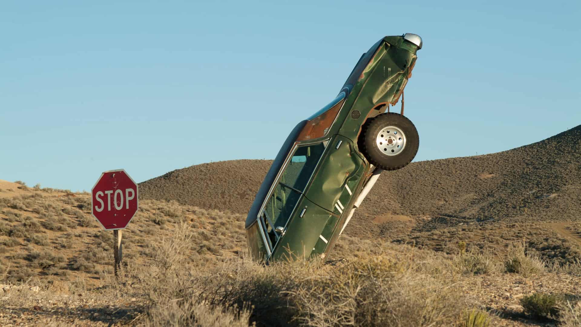 An old rusted car has nose dived from the sky to crash in the barren desert.