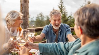 A group of older women and men cheers their wine glasses ecstatically, even though they're in lockdown.