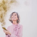 An older women receives good news with golden sparkles and glitter shooting out of her phone.