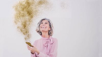 An older women receives good news with golden sparkles and glitter shooting out of her phone.