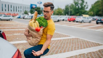 A man with a bag of groceries tries to catch an apple that has fallen out.