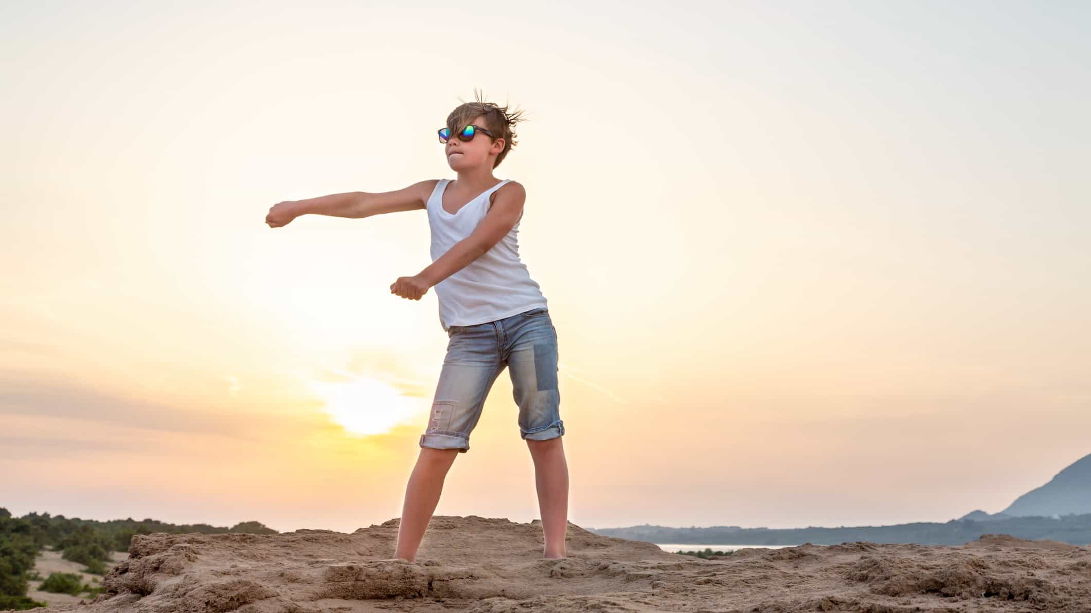 A teenage boy dances at sunset on the beach, moving his arms and hips to the beat.