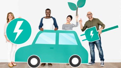 A group of four people pose behind a graphic image of a green car, holding various symbols of clean electric, lithium powered energy including energy symbols and a green plant representing the rising Vulcan Energy share price