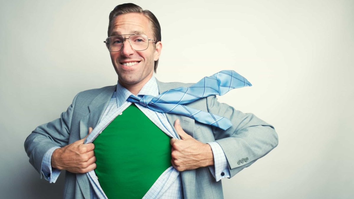 A wide-smiling businessman in suit and tie rips open his shirt to reveal a green t-shirt underneath