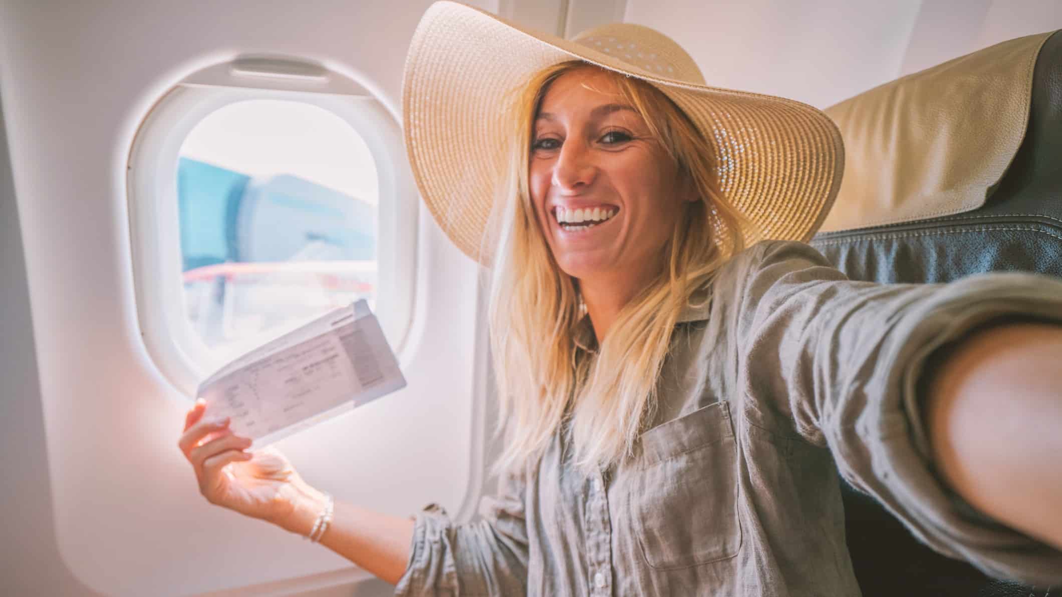 a happy passenger sits in her airplane seat with boarding pass in hand smiling widely at the prospect of travel.