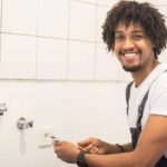 a happy plumber smiles while repairing bathroom fittings in a home.