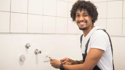 a happy plumber smiles while repairing bathroom fittings in a home.