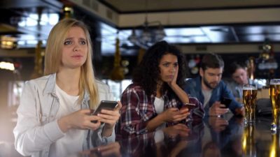 two sad gamblers with mobile phones look dejected at a bar with mobile phones in hand