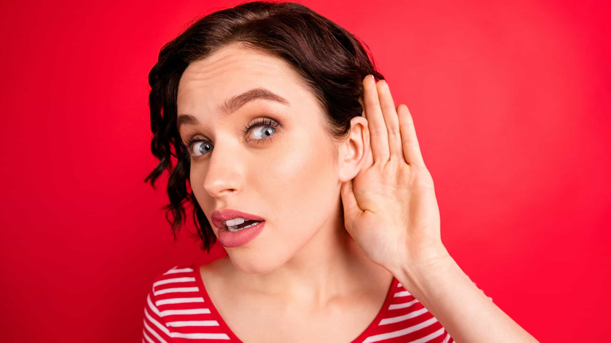 a woman leans forward with her hand behind her ear, as if trying to hear information.