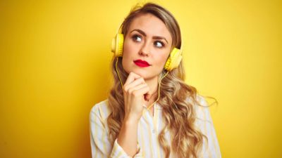 person with large headphones looking puzzled holding their hand to their chin.