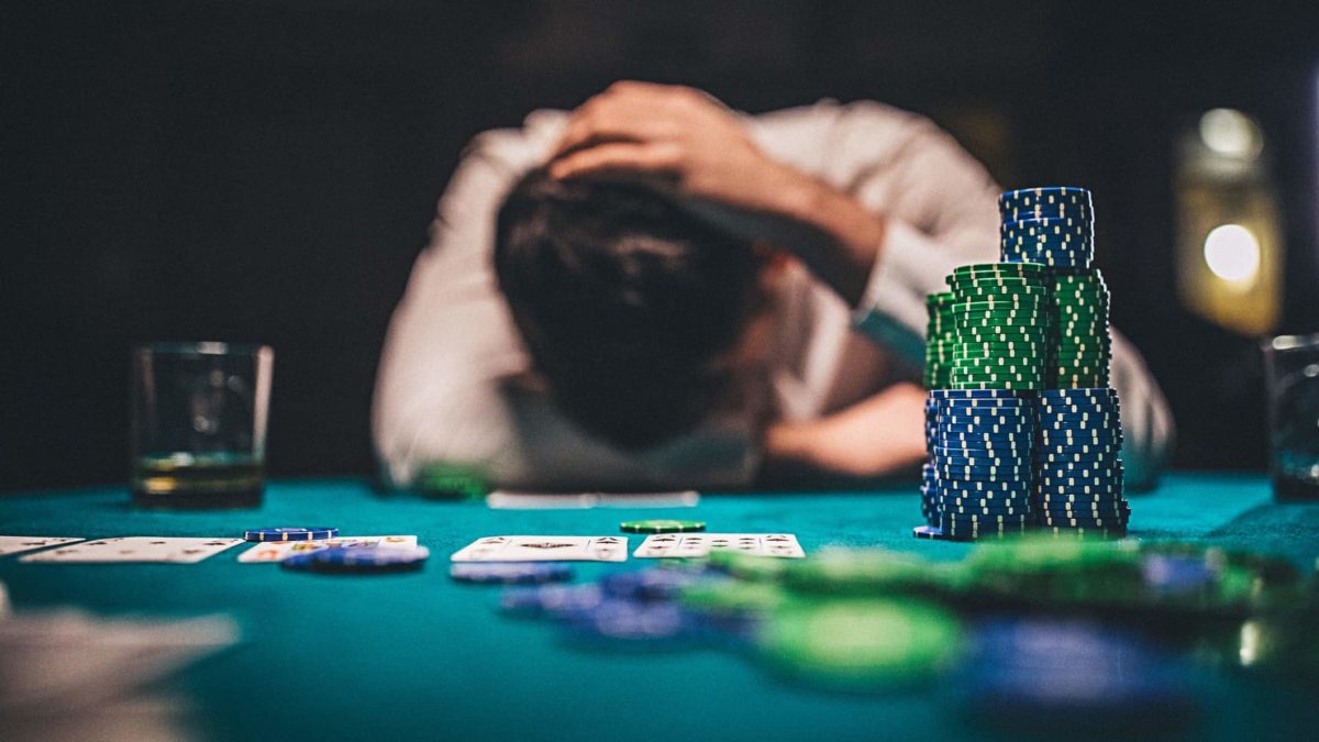 a sad gambler slumps at a casino table with hands on head and a large pile of casino chips in the foreground.