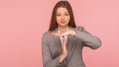 a woman in a business suit makes the hand signal in the shape of a time to represent time out, representative also of a trading halt