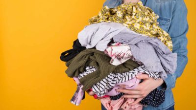 a woman holds a pile of old clothes for recycling.