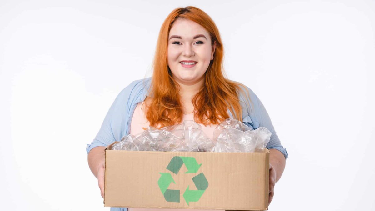 a person holds a cardboard box with a recycling symbol containing plastic packaging material.