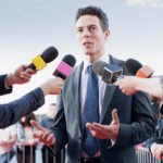 A man giving an interview before several handheld media microphones.