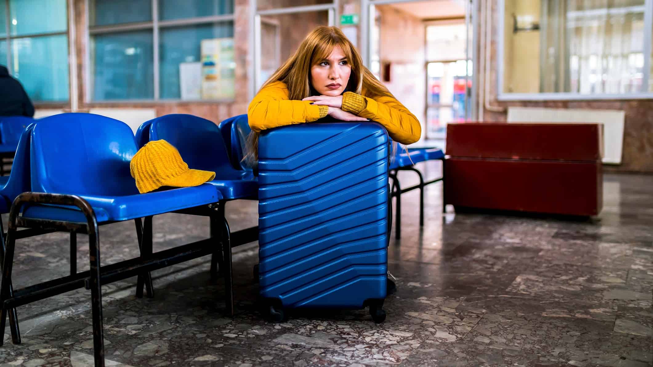 a sad woman sits leaning on her suitcase in a deserted airport lounge