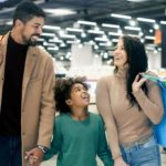 a family with shopping bags walks inside a shopping mall with shops in the background.