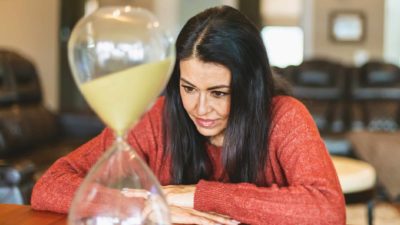 a woman watches sand pass through an hourglass.