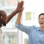 co-workers wearing headphone and microphones high five in celebration of good news in an office setting.