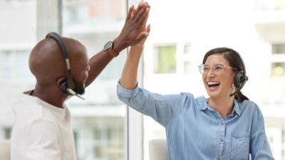 co-workers wearing headphone and microphones high five in celebration of good news in an office setting.