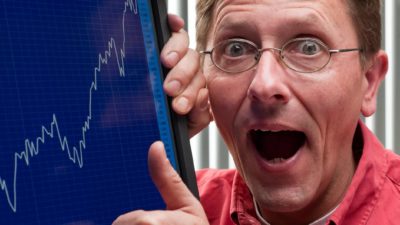 a happy investor with wide mouth expression grasps a computer screen that shows a rising line charting the upward trend of a share price