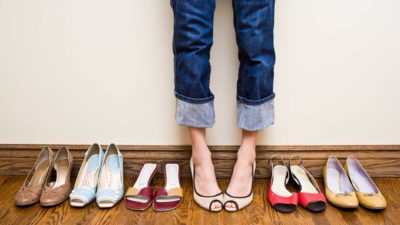 a shoe collection lined up with a person's feet in a pair of shoes in the middle of the line up.