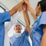a group of doctors and medical staff in uniform high five in celebration in a hospital setting