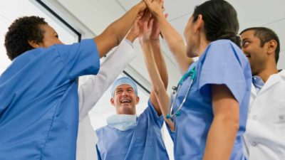 a group of doctors and medical staff in uniform high five in celebration in a hospital setting