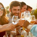 A group of people clink wine glasses in an outdoor, late afternoon setting to celebrate the rising Treasury Wine share price