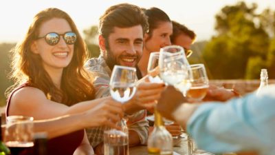 A group of people clink wine glasses in an outdoor, late afternoon setting to celebrate the rising Treasury Wine share price