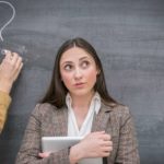 person thinking with another person's hand drawing a question mark on a blackboard in the background.