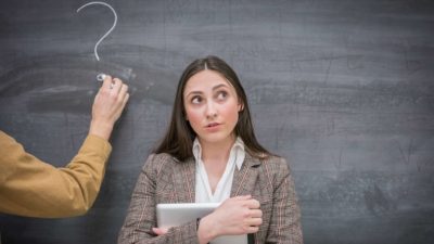 person thinking with another person's hand drawing a question mark on a blackboard in the background.