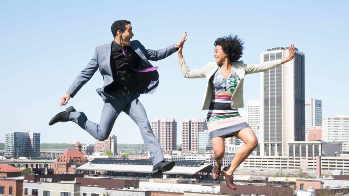 two people celebrating good news high five each other while jumping in the air with a city landscape in the background.