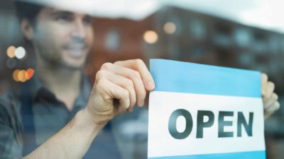 a man turns over an open sign in a window, signifying open for business.