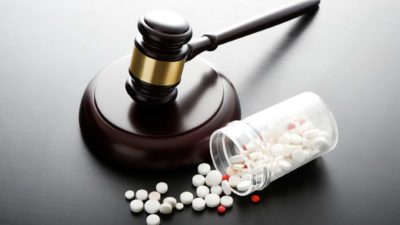 a legal gavel rests near a bottle of pharmaceutical pills with the contents spilling onto the desk.