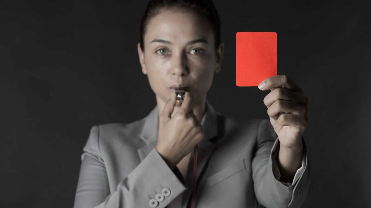 a woman in business attire is blowing a whistle and holding up a red card, referring to a sporting analogy for sending someone off the field for disciplinary reasons.